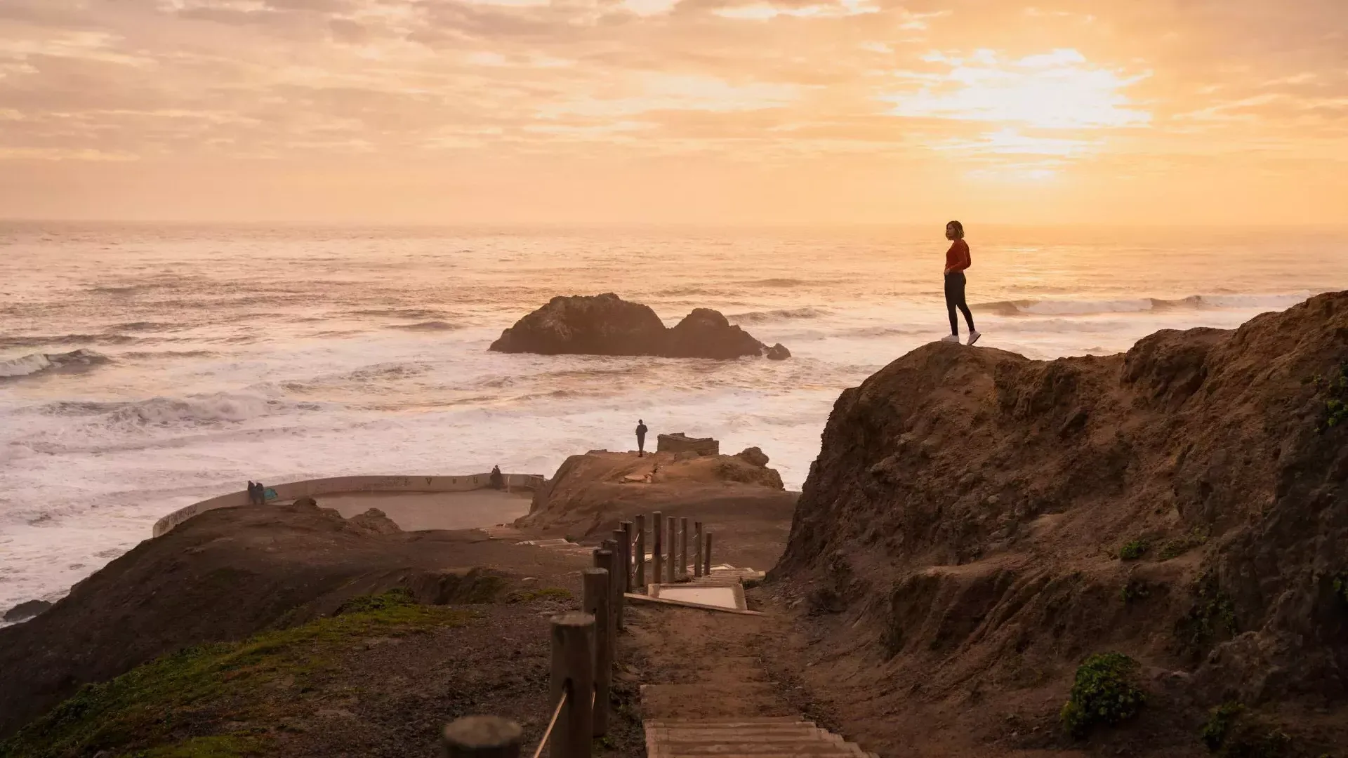 Two people stand on rocks overlooking the ocean at Sutro Baths in San Francisco.