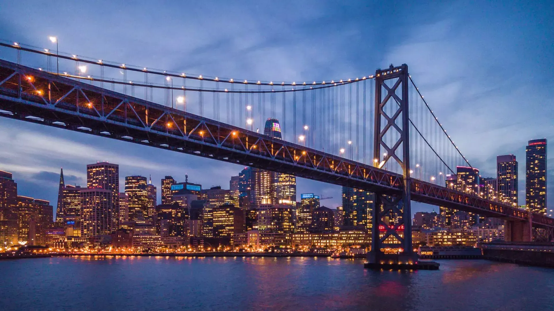 Il Bay Bridge e il lungomare dell'Embarcardero si illuminano di notte.