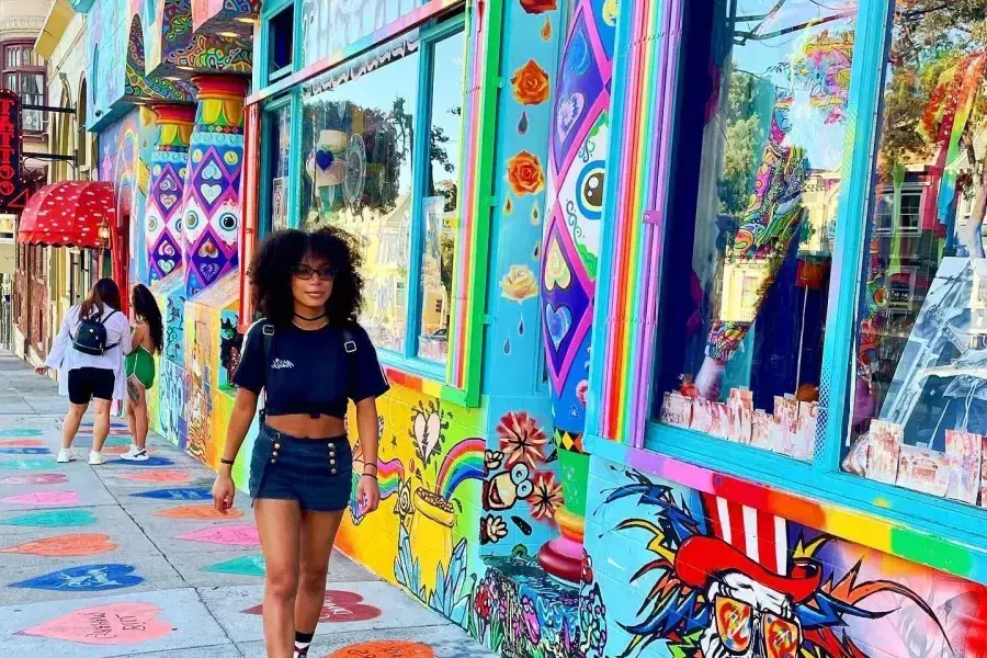 A woman walks down a street with colorful buildings in San Francisco's Haight-Ashbury neighborhood.