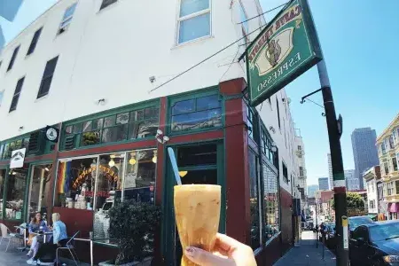 A person's hand holds a coffee drink with the exterior sign and storefront of 咖啡的里雅斯特 in the background.