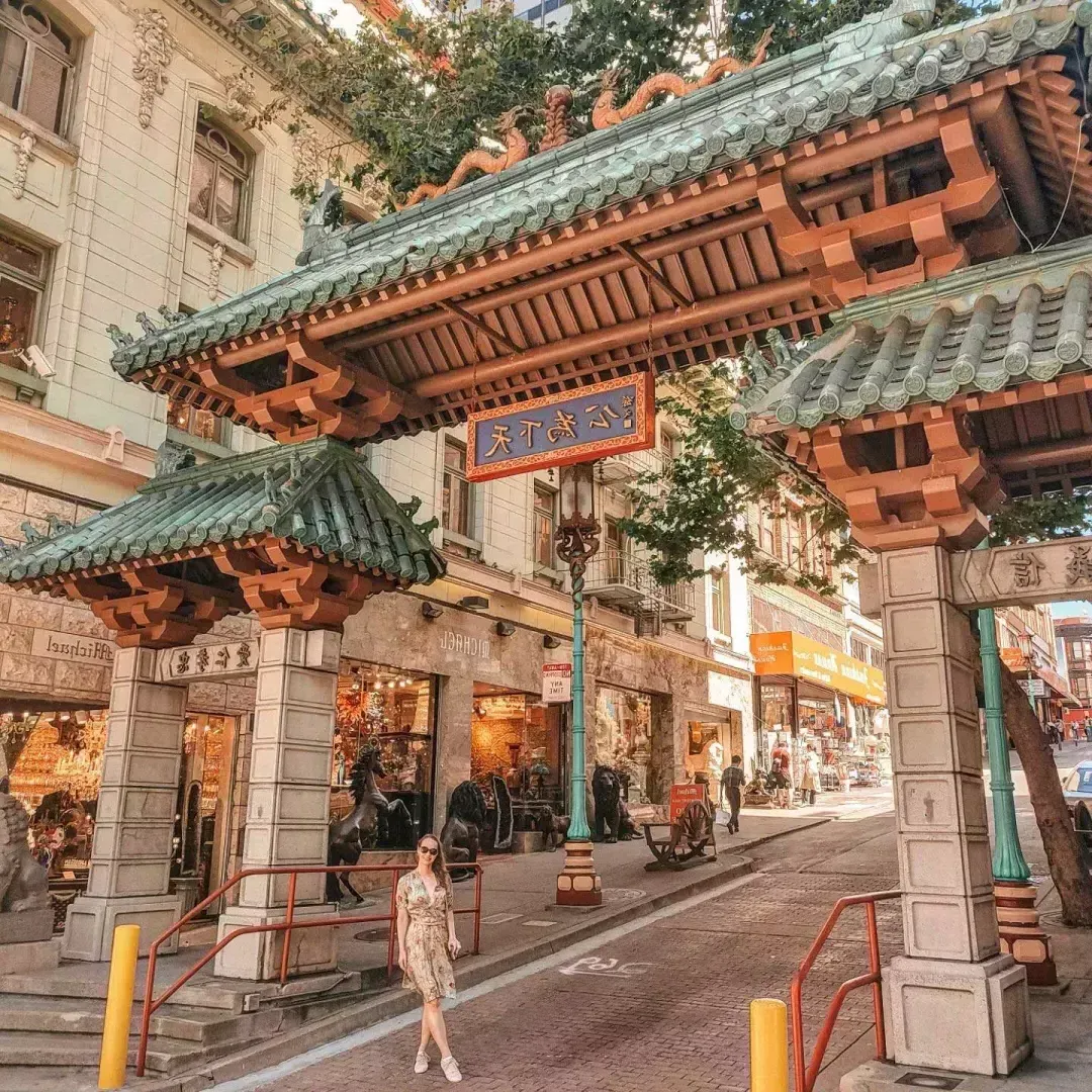 A woman poses in front of an ornate gate marking the entrance of San Francisco's Chinatown.