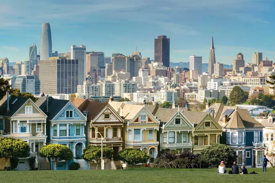 Os piqueniques sentam-se na grama do Alamo Square Park com as 画现在 e o horizonte de São Francisco ao fundo.