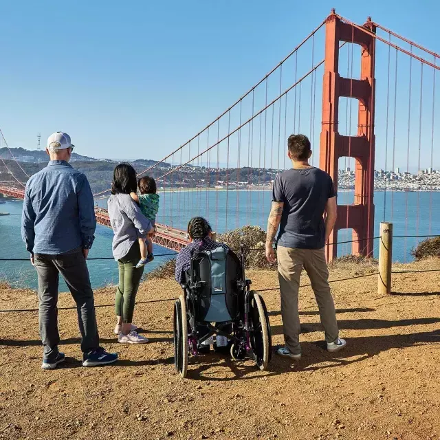 一群人, 包括一个坐轮椅的人, est vu de dos alors qu'ils regardent le 金门大桥 depuis Marin Headlands.