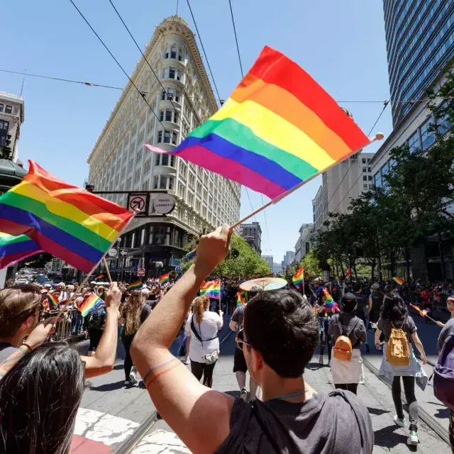 People walking in the San Francisco Pride parade wave rainbow flags.